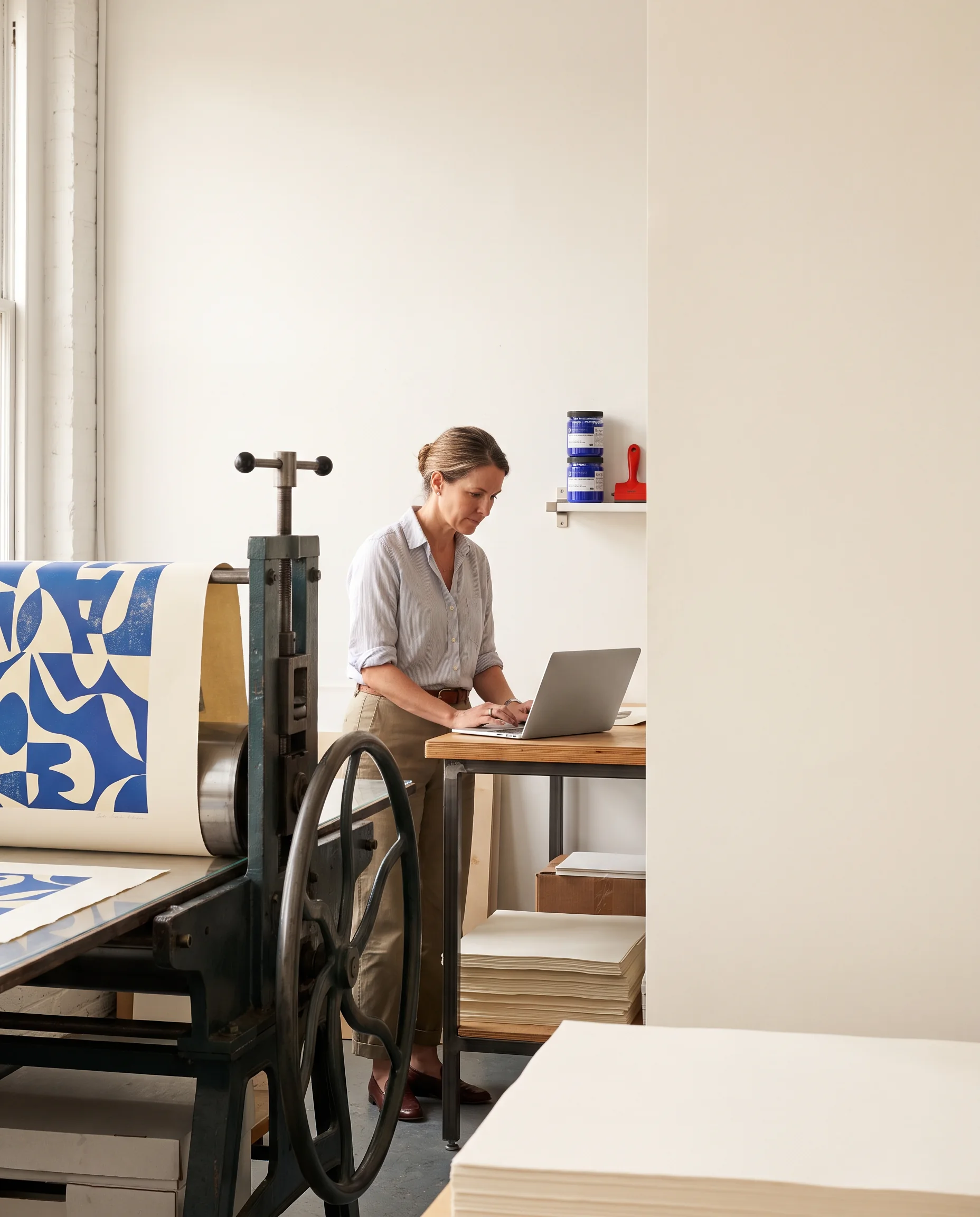 A printmaker working beside a press and laptop