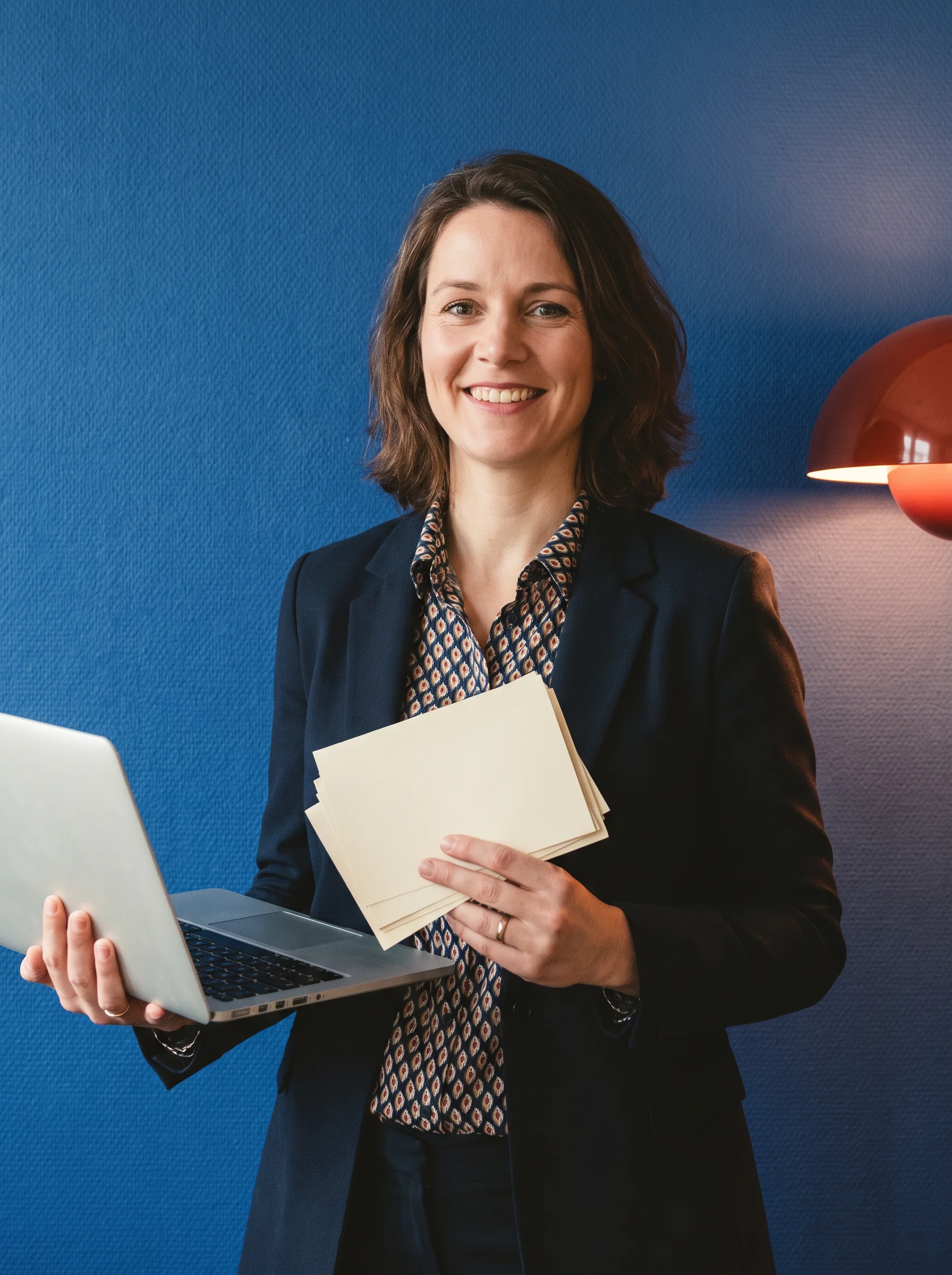 Person holding a laptop and paper cards against an ultramarine wall